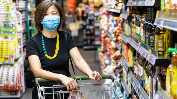 Asian woman shopping groceries in supermarket with protective face mask as new normal requirement