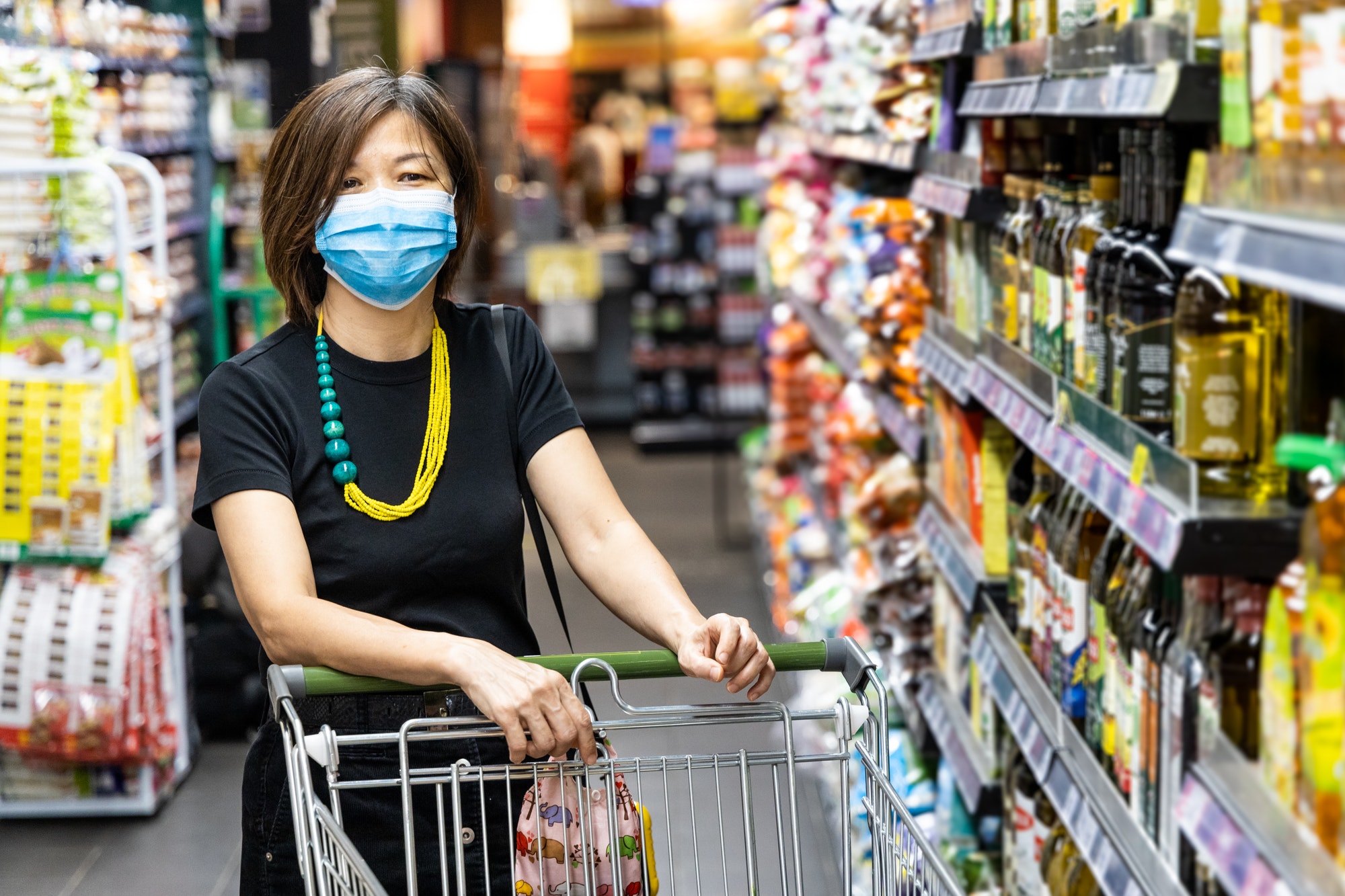 Asian woman shopping groceries in supermarket with protective face mask as new normal requirement